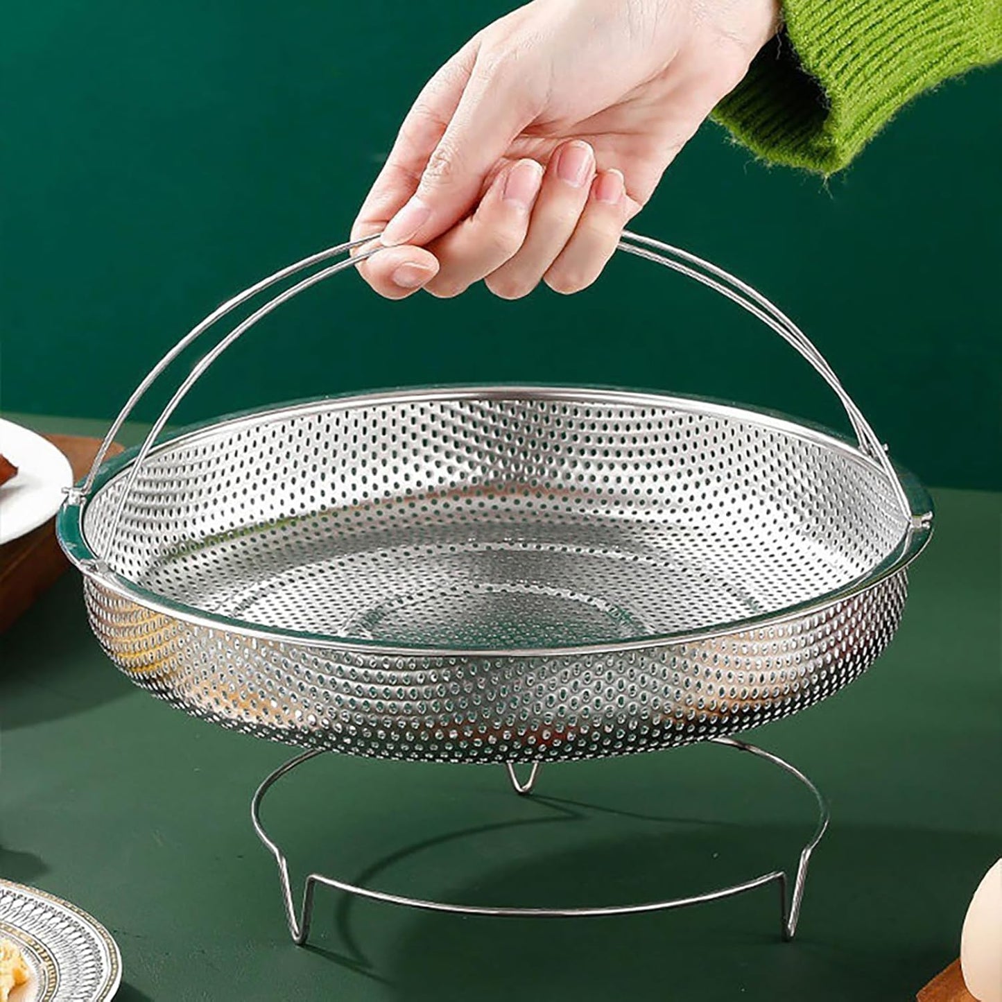 Metal steamer basket held by a hand on a green background