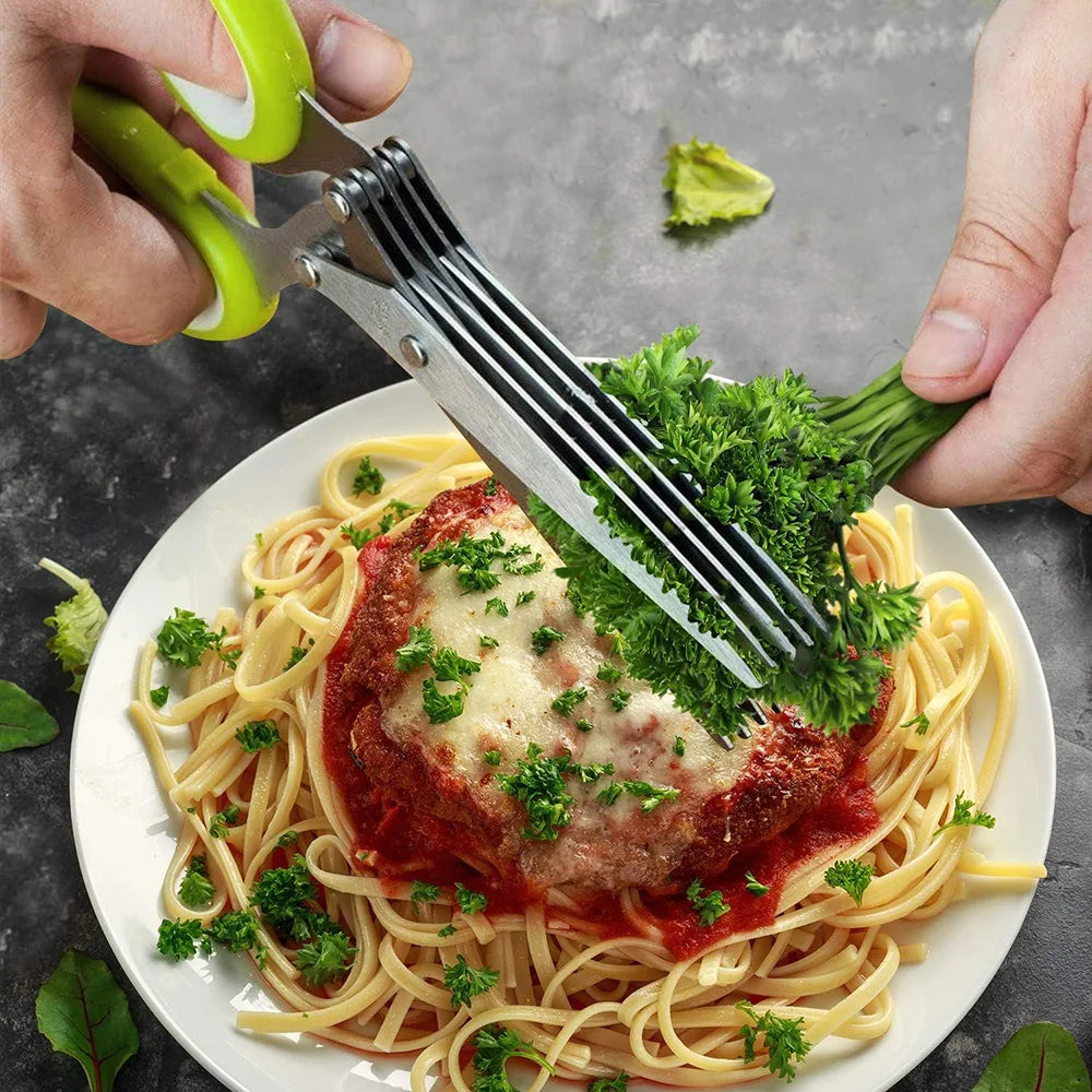 Person using kitchen shears to cut greens over a plate of spaghetti with meatballs.