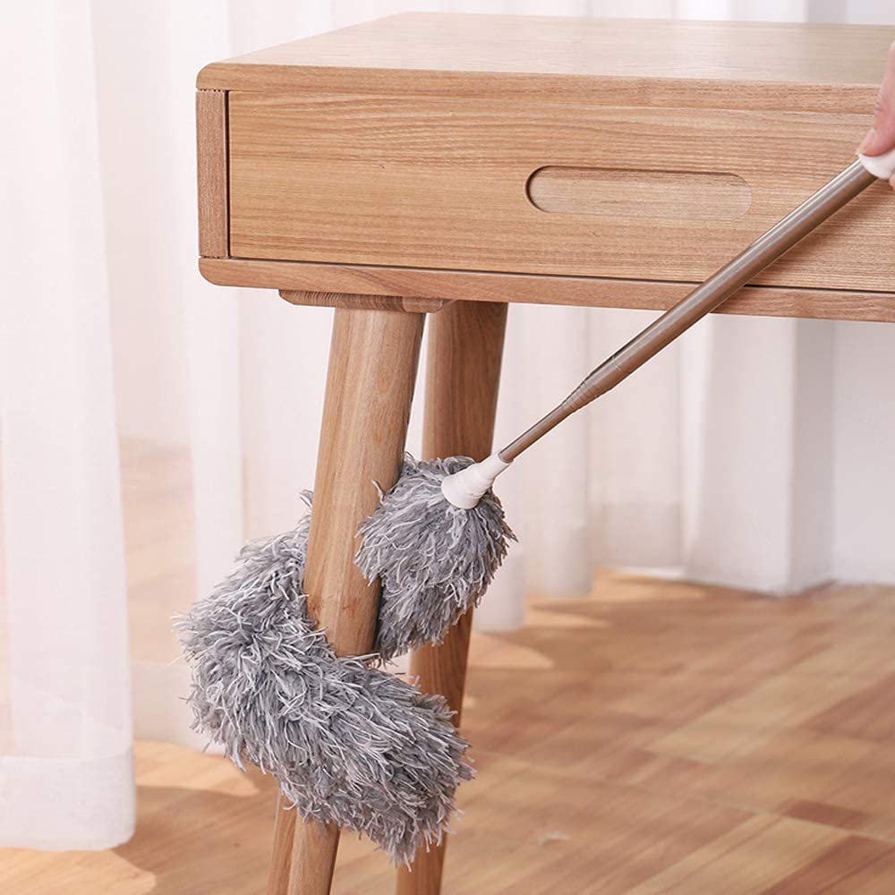 Person using a duster to clean a wooden table.