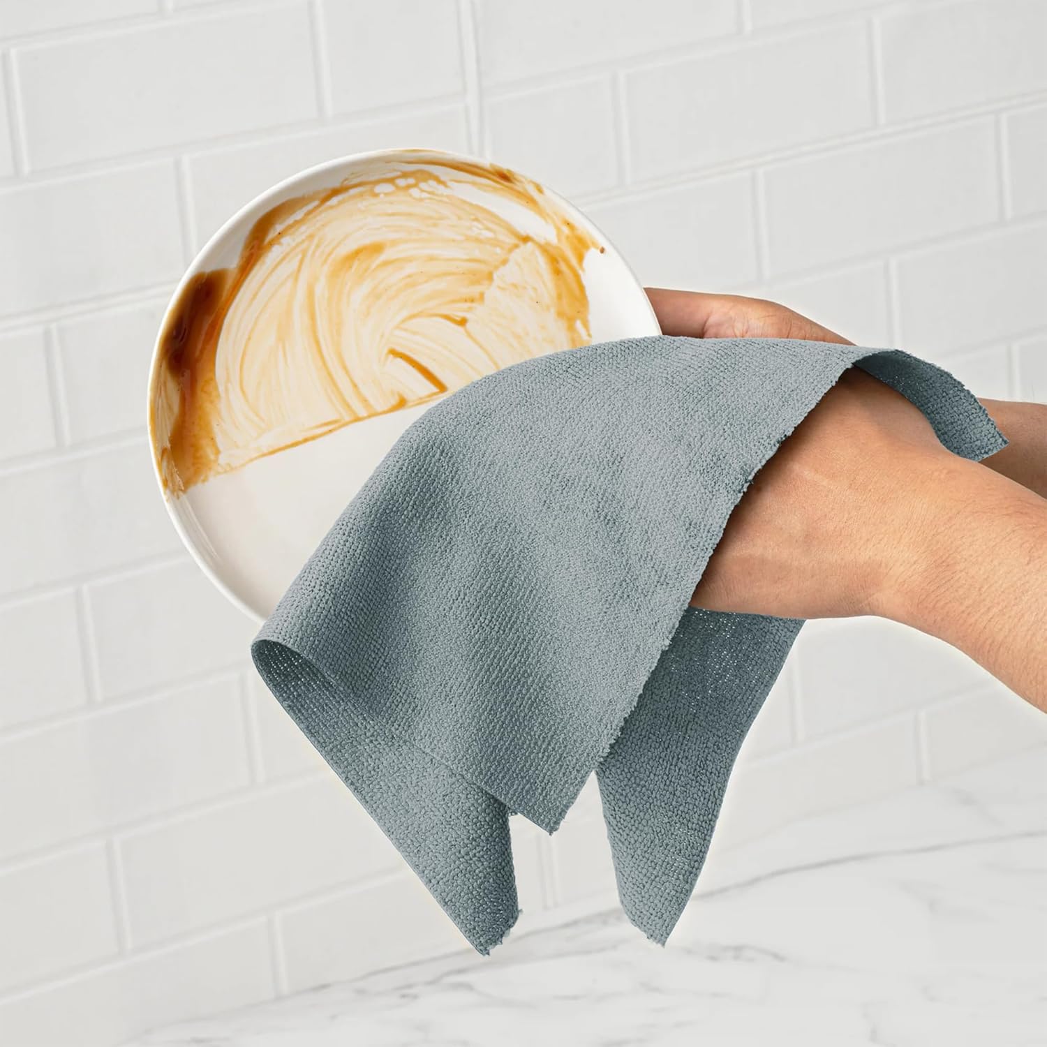 Person holding a blue towel over a plate with a coffee design on a tiled wall background