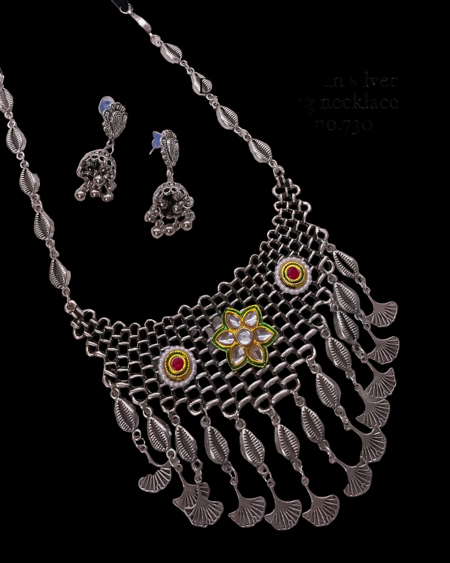 Silver necklace with floral design and red stones on a light gray background